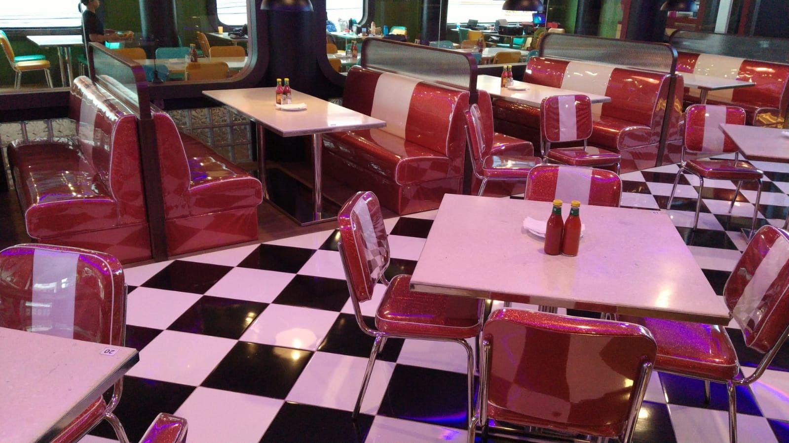 Ruang makan restoran dengan deret booth berlapis merah putih, meja, dan lantai kotak-kotak hitam putih.