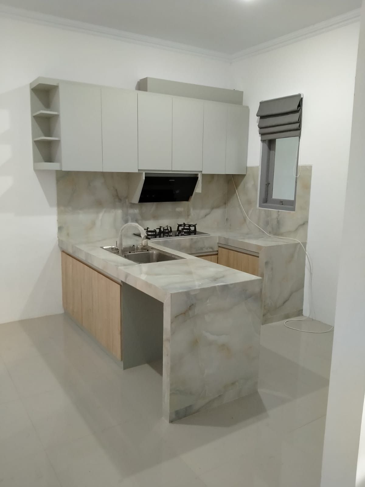 Kitchen set putih dengan meja dan backsplash bermotif marmer serta meja penyiapan yang menjorok ke ruang.