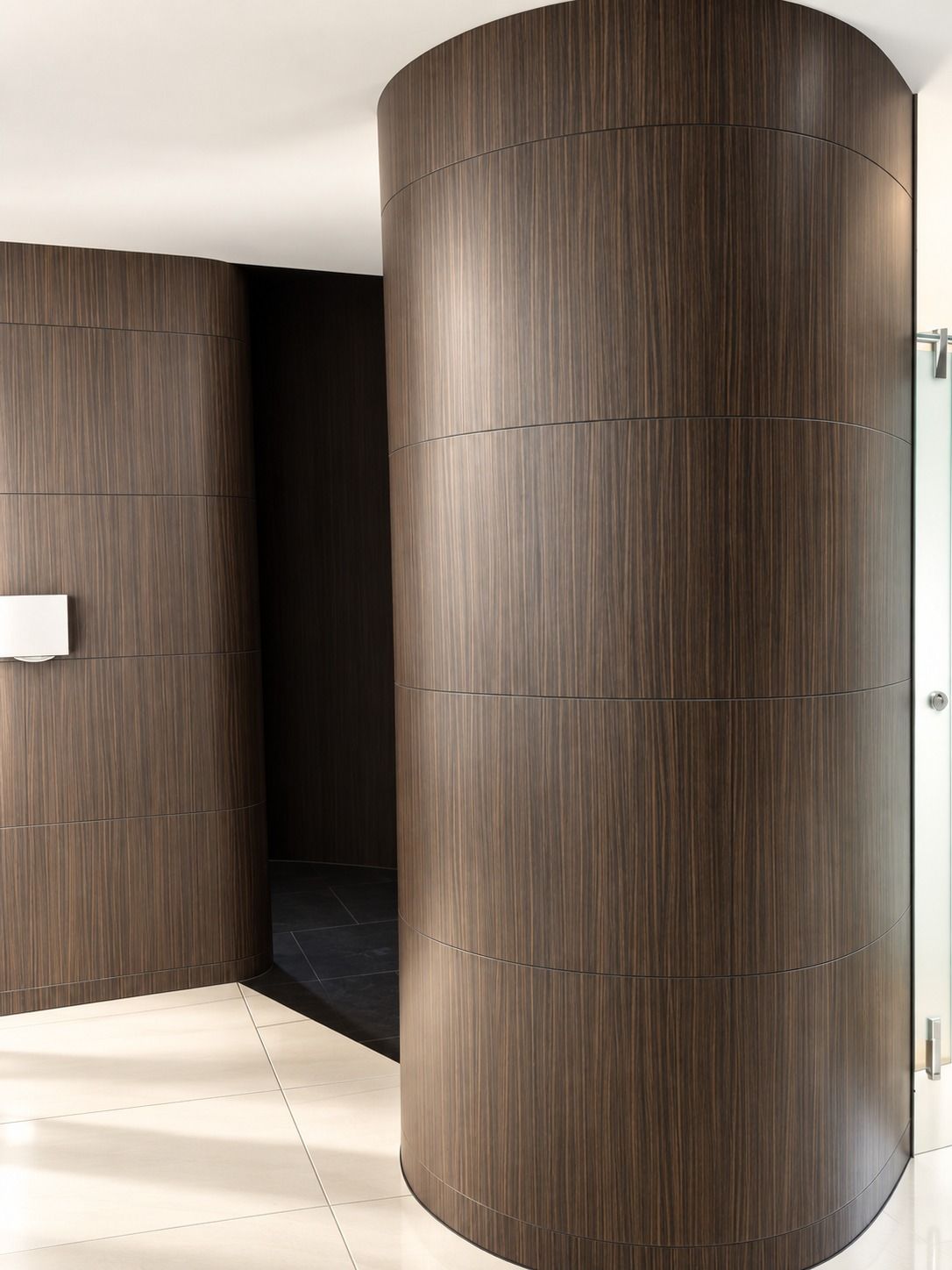 Kolom bulat yang dibungkus panel bermotif kayu gelap di dalam area toilet.