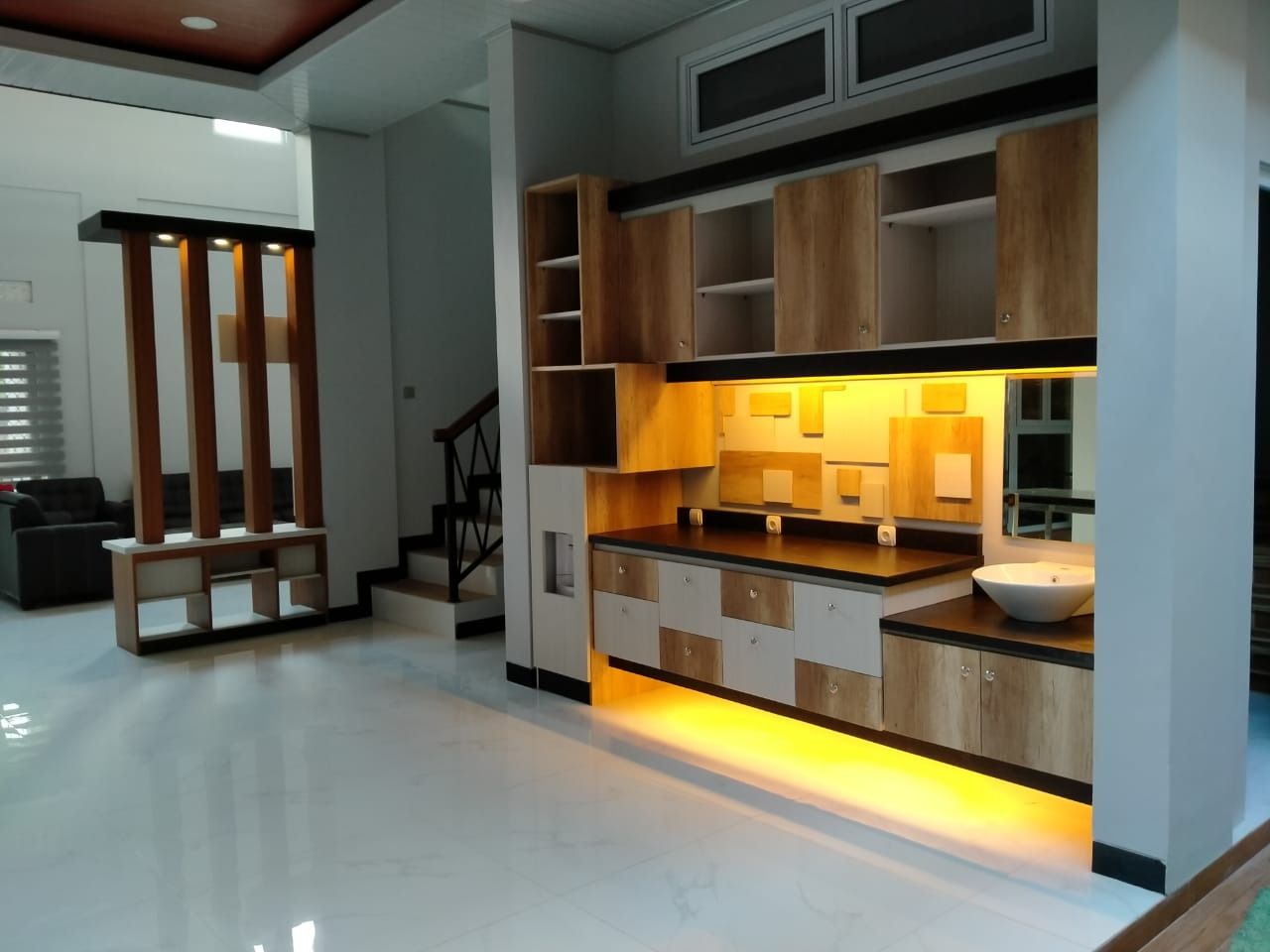 Kabinet pantry dengan laci dua warna dan lampu tersembunyi di bawahnya, bersebelahan dengan partisi bertiang kayu.