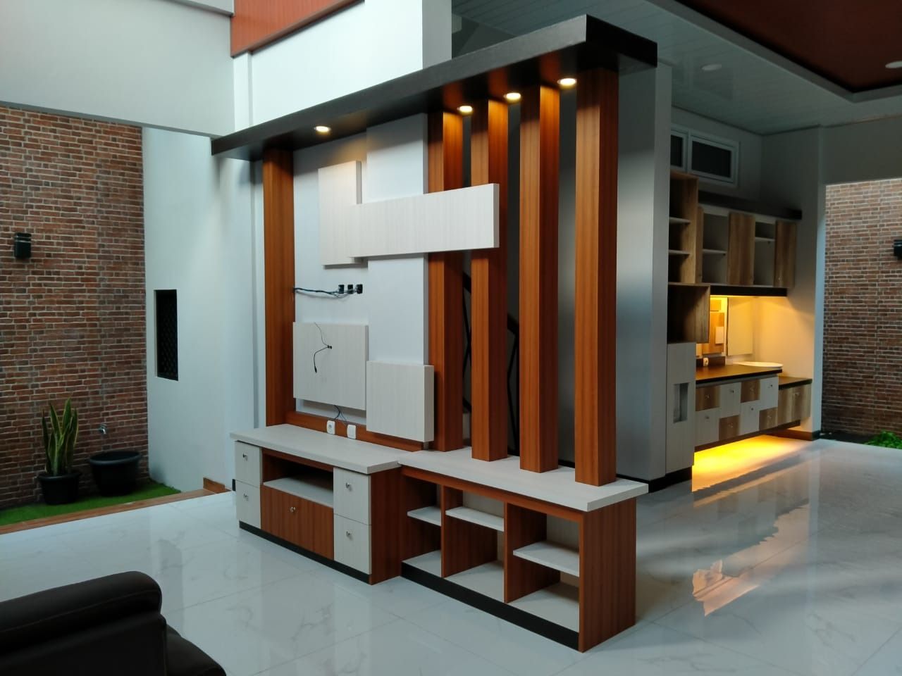 Partisi bertiang kayu dengan unit TV dan rak terbuka di sisi ruang keluarga.