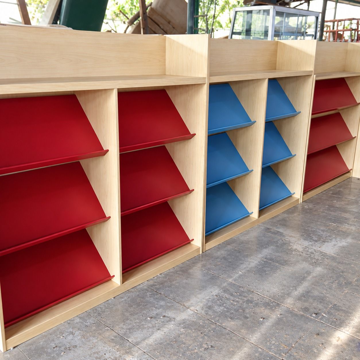 Beberapa unit rak majalah dengan papan miring merah dan biru, berjajar di workshop sebelum dikirim.
